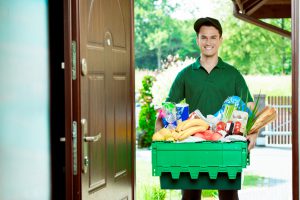 Delivery man standing at the door of the house and carrying box with groceries, smiling at camera.
